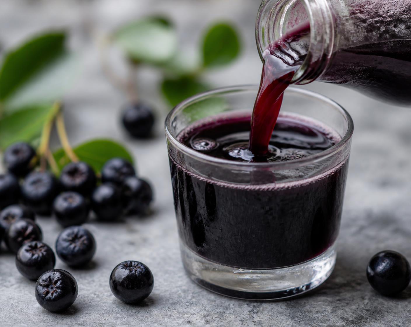 Unsweetened Aronia juice poured into a tasting glass beside loose berries and leaves
